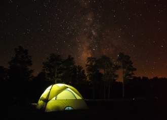 A glowing green tent in a starry wooded area