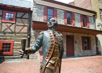 Historic statue of a colonial man outside of a two-story, stone building
