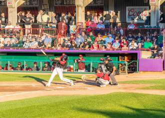 A baseball player swinging a bat in front of a dugout with people in the stands above