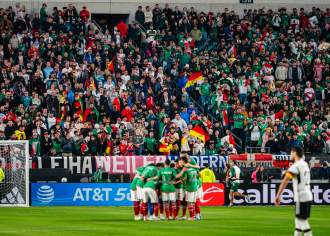 A huddle of soccer players in front of a goal in a crowd-filled stadium