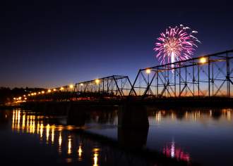 Fireworks bursting at night over a bridge on a river