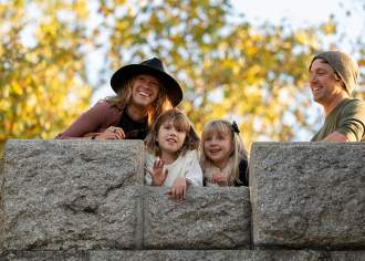 A man and a woman peering over a stone wall with two small girls