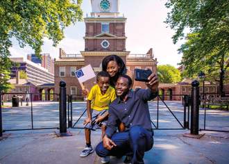 A man posing for a selfie with a woman holding a small American flag and a young boy in front of a historical building