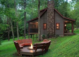 Exterior of a rustic, wood cabin with a fire pit outside and two red benches around it