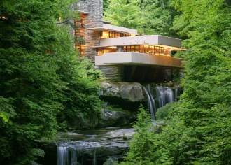 A modern home sitting on top of a waterfall with green trees surrounding it