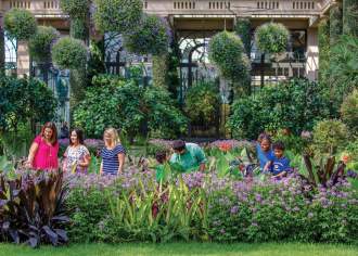 A group of adults and kids looking at tall flower beds in a conservatory