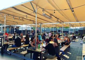 People sit at picnic tables under a large tent enjoying beers