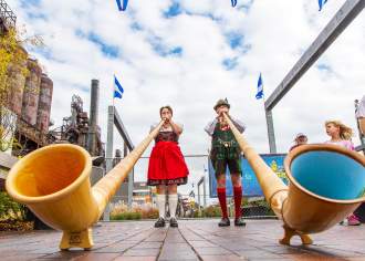 A man and woman in traditional German attire playing large trumpets on a stage