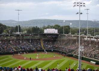 A baseball stadium filled with people watching a baseball game. A sign on the top of the stadium reads Welcome to Howard J. Lamade Stadium