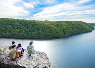 A group of four hikers sitting and kneeling on an overlook above a lake on a sunny day