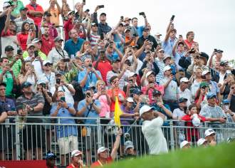 People in stand watching a person hit a golf ball with a club