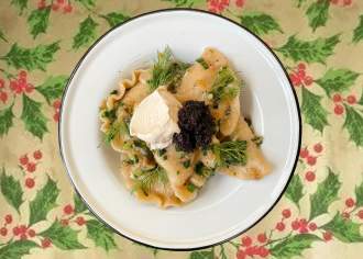 A plate of pierogies with garnish set on a decorative table cloth with holly