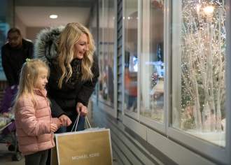 Woman and young girl holding shopping bags and looking into a storefront decorated for the holidays