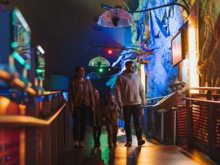 A family of four, including two young children, walks through The Deep, looking at a colourful exhibit with  skeletons and educational displays mounted on the walls.
