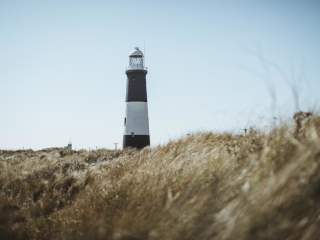 Spurn Point's black and white light house standing above tall dune grass blowing in the wind under a bright blue sky