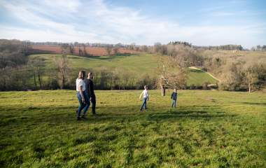 Two boys walk ahead of their parents across a field near Blockley, with trees and hills in the distance.