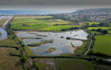 Aerial view of a scenic wetland area with ponds, surrounded by vibrant green fields and distant hills. A tranquil landscape under a clear sky.