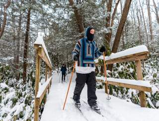 Two people in winter gear cross country skiing across a snow-covered, wooden bridge in the Laurel Highlands