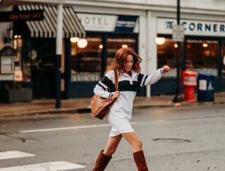 A woman in tall boots carrying a purse walking across a cross walk in a street