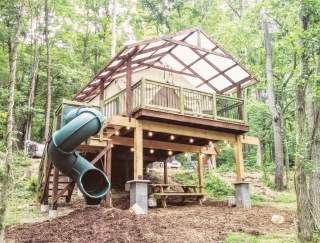 A large treehouse with a winding slide attached to it in the woods