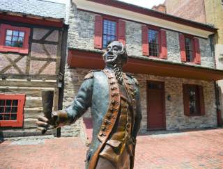 Historic statue of a colonial man outside of a two-story, stone building