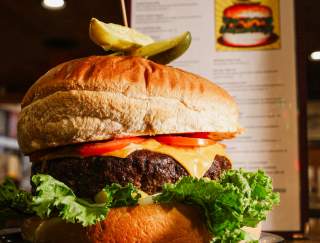 A large, beef burger with a toothpick and pickle on top