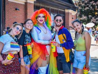 Four people posing with a drag queen at a street parade