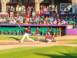 A baseball player swinging a bat in front of a dugout with people in the stands above