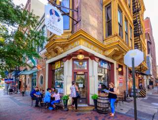 The exterior of a storefront on the corner of a street intersection with people sitting outside and walking in the store