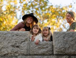 A man and a woman peering over a stone wall with two small girls