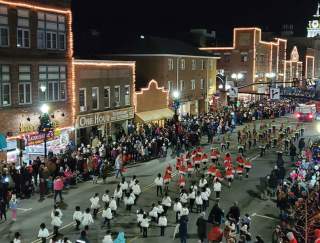 A main street at night with a parade and Christmas lights decorating the town