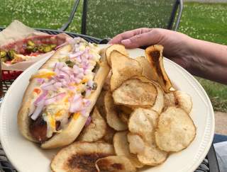 A plate of a loaded hot dog with chips