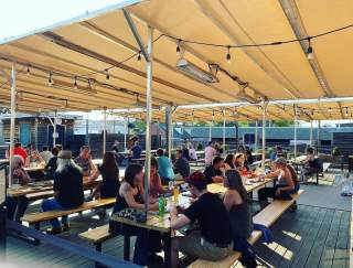 People sit at picnic tables under a large tent enjoying beers