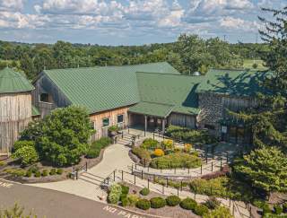 Birds eye view of a wooden barn with a green roof and a parking lot in front