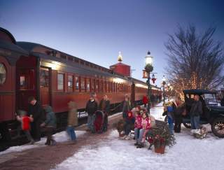 Adults and small children boarding the historic Strasburg Rail Road with snow on the ground and Christmas decorations throughout