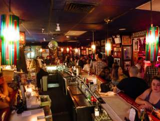 A crowd of festive people sitting and standing inside, along the bar, in Philly.