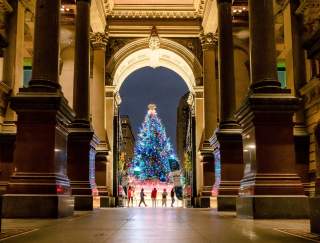 An archway through a historic building with people standing in front of a glowing Christmas tree in the distance