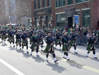 A group of men in Irish attire marching in a street parade with bag pipes