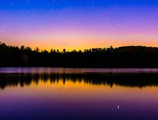 Blue and orange ombre night sky over a lake with trees