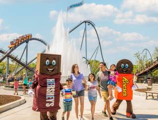 A family of five walking with two mascots in an amusement park