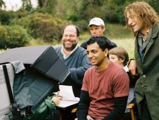 A director sitting in a chair looking at a camera with his staff standing around
