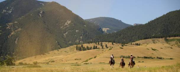 Horseback riders in grassy field with mountain ranges in the background.