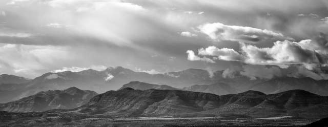 a black and white photo of sprawling mountain ridges in the distance beneath swirling white clouds