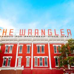 A photo of the red and white brick building with the famous "The Wrangler: Famous for Ranchwear Since 1934".