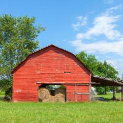 A Southern red barn filled with hay bales with a bright blue sky as a backdrop in Landrum, SC.