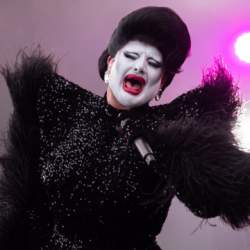 A drag artist on stage wearing an impressive black outfit