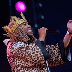 A member of the cast stands on stage wearing a gold crown and leopard print boxing gown