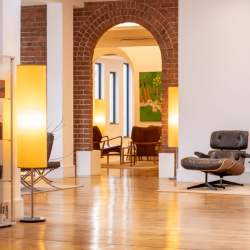 A modern, light lobby space with white walls, light oak flooring, an exposed brick archway and minimal decor and furnishings.