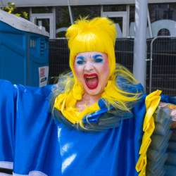 A drag queen with yellow hair and a blue and yellow outfit