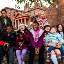 Kids and an adult sitting together at the Royal Albert Dock, smiling at the camera